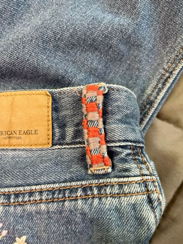 A close view of a worn denim waistband, its leather patch faded and a friendship bracelet knotted round the belt loop.
