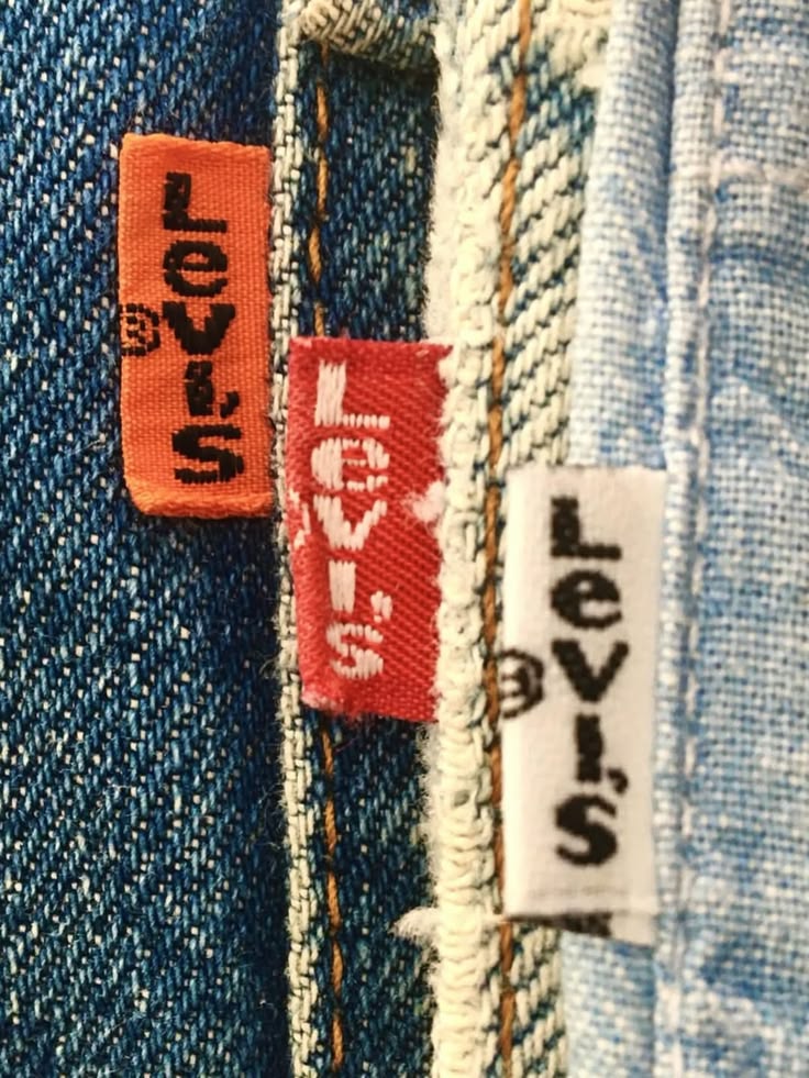Three woven Levi's tabs — orange, red and white — on the seams of different pairs of denim.