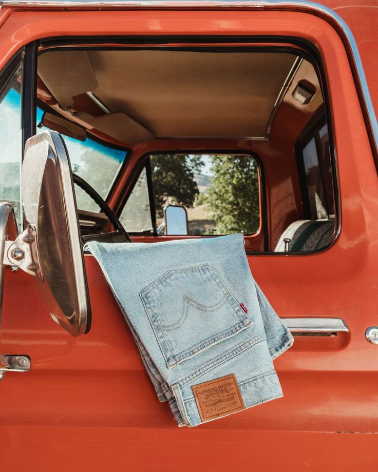 A folded pair of light-wash jeans resting on the door of a red pickup truck.