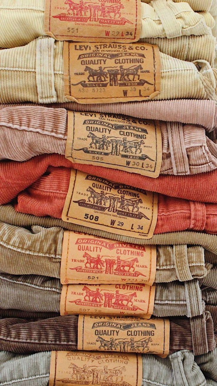 A stack of folded vintage corduroy trousers, their leather waistband patches facing out.